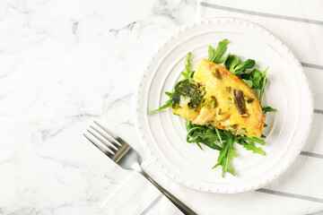 Tasty vegetable casserole, arugula and fork on white marble table, top view. Space for text