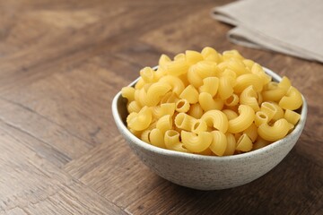 Raw horns pasta in bowl on wooden table, closeup