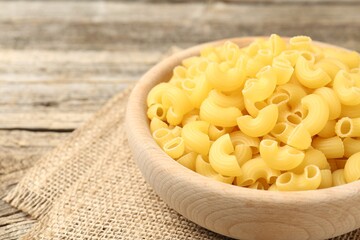 Raw horns pasta in bowl on wooden table, closeup. Space for text