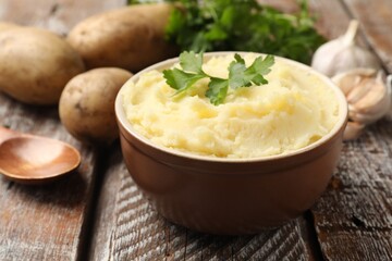Delicious mashed potato with parsley, garlic and spoon on wooden table, closeup