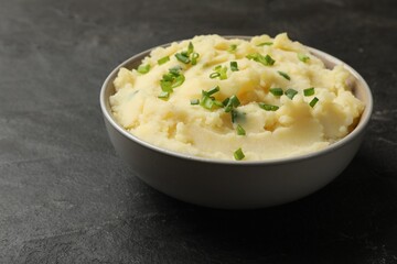 Delicious mashed potato with green onions in bowl on black table, closeup. Space for text