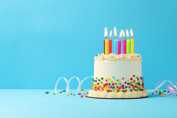 Delicious bento cake with colorful sprinkles, burning candles and serpentine streamers on light blue table. Space for text