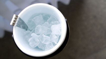 White ice bucket with metal tongs holding refreshing ice cubes