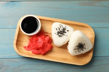 Rice balls (onigiri), soy sauce and pickled ginger on light blue wooden table, top view....