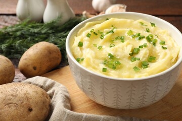 Tasty mashed potato with green onion in bowl and raw vegetables on wooden table, closeup