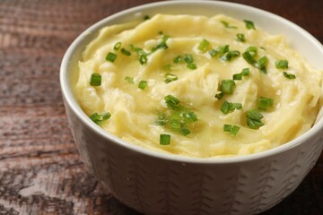 Tasty mashed potato with green onion in bowl on wooden table, closeup
