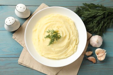 Tasty mashed potato with dill in bowl, garlic and spices on light blue wooden table, flat lay