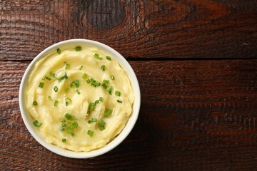 Tasty mashed potato with green onion in bowl on wooden table, top view. Space for text