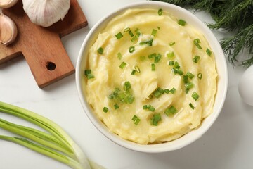 Tasty mashed potato with green onion in bowl and dill on white table, flat lay