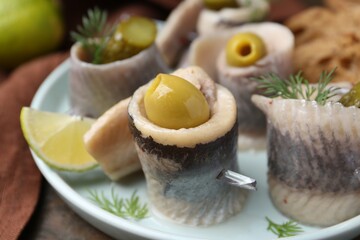 Delicious herring rolls with olives, pickles and dill on table, closeup