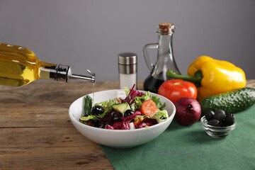 Woman pouring oil onto salad at wooden table against grey background, closeup