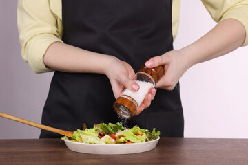 Woman salting tasty salad at wooden table against white background, closeup
