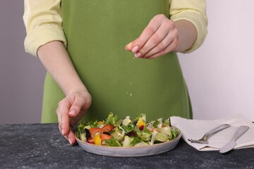 Woman salting tasty salad at dark textured table against white background, closeup
