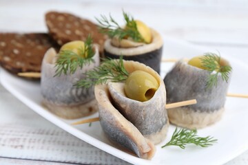 Delicious herring rolls with olives, dill and bread on white wooden table, closeup