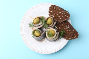Delicious herring rolls with olives, dill and bread on light blue background, top view