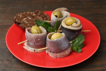 Delicious herring rolls with olives, parsley and bread on wooden table, closeup