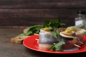 Delicious herring rolls with olives and parsley on wooden table, closeup. Space for text