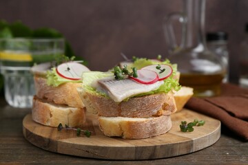 Tasty sandwiches with herring, radish and lettuce on wooden table, closeup