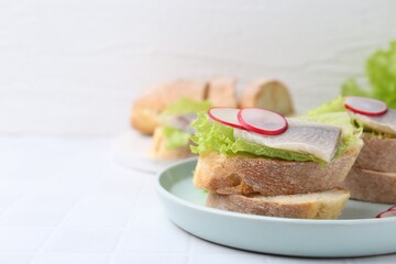 Tasty sandwiches with herring, radish and lettuce on white tiled table, closeup. Space for text