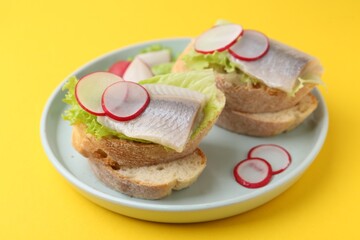 Tasty sandwiches with herring, radish and lettuce on yellow background, closeup