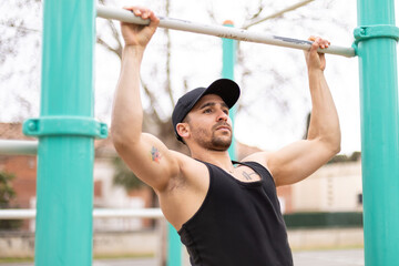 Young man doing pull-ups on outdoor fitness bar.