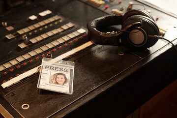 Badge of young female reporter and headphones lying on sound mixing console in studio or TV van for...