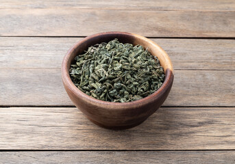 Dried green tea leaves on a bowl over wooden table