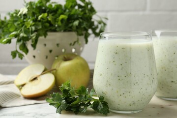 Healthy parsley drink in glasses, leaves and apples on white marble table, closeup
