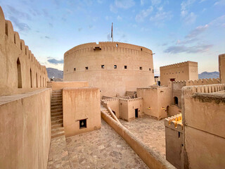 Nizwa Fort, Oman - Ancient circular fortification with crenellated walls and towers under a cloudy...