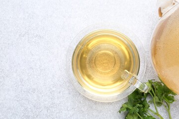 Aromatic herbal tea in glass cup, fresh parsley and teapot on light grey table, flat lay. Space for text
