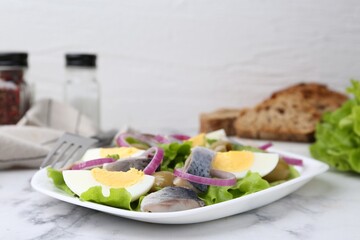 Delicious salad with herring, egg and vegetables on white marble table, closeup