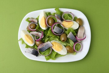 Delicious salad with herring, egg and vegetables on green background, top view