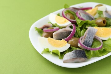 Delicious salad with herring, egg and vegetables on green background, closeup. Space for text