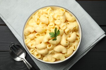 Delicious macaroni and cheese with parsley served on black wooden table, top view