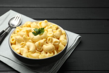Delicious macaroni and cheese with parsley served on black wooden table, closeup. Space for text
