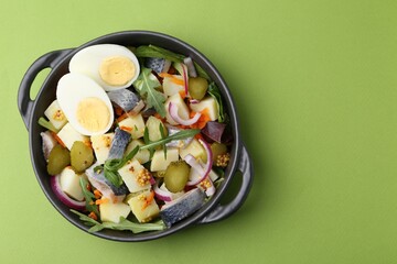 Delicious salad with herring, egg and vegetables in bowl on green background, top view. Space for...