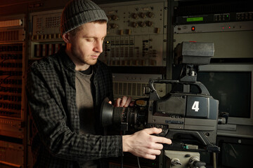 Young man pressing power button on professional video camera while preparing equipment for shooting...