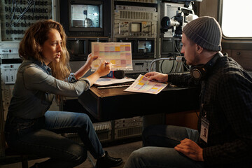 Young confident woman explaining information in schedule to colleague from production team while...