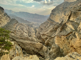 Breathtaking Landscape of Rugged Mountain Cliffs and Deep Canyon in Jebel Shams, Oman - Scenic View of Rocky Terrain and Dramatic Sky in Middle Eastern Wilderness (177 characters)