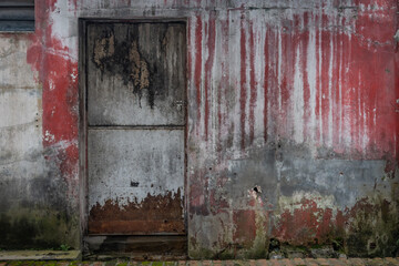 A dirty, peeling wall in shades of red, brown, and gray, with a locked metal door, creating a grunge aesthetic