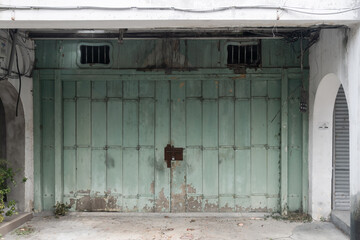 A photo of a dilapidated, closed wooden gate in pastel green shades with peeling paint and an iron...