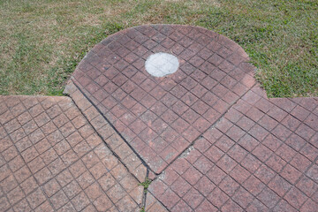 Street paving in reddish-brown color, surrounded by grass and a flat, painted white circle, arranged to form a geometric figure
