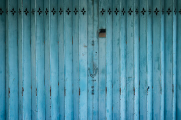 A close-up view of a dilapidated azure blue metal accordion-style gate.