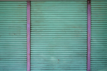 A close-up view of a dilapidated garage door in a green tint with purple iron bars dividing it
