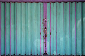 A dilapidated, closed garage door in a green tint with purple iron bars dividing it, featuring three locks