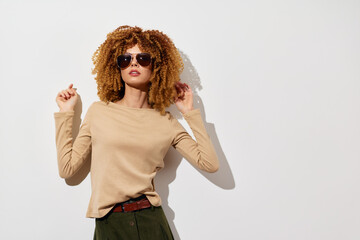 Fashionable model posing against a plain white background, wearing sunglasses and a beige long...