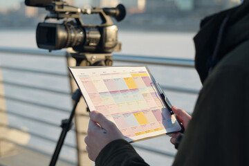 Hand of young unrecognizable male operator holding paper document with schedule of video shootings...