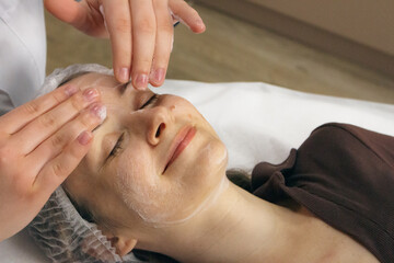 Foam cleaning and face massage in beauty salon. Smiling woman relaxing with anti-aging massage. Wellness procedure. Skincare treatment. Cosmetologist hands over client face. Healthcare pleasure. 