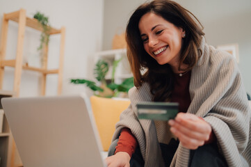 Smiling woman using laptop and credit card for online shopping at home