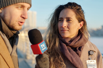 Young confident woman with microphone looking at male politician responding questions of interview...